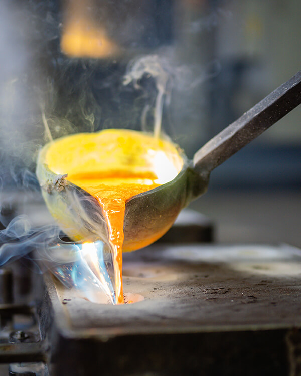 Geschmolzenes Metall aus Kelle gegossen, Rauch und blaue Flammen.