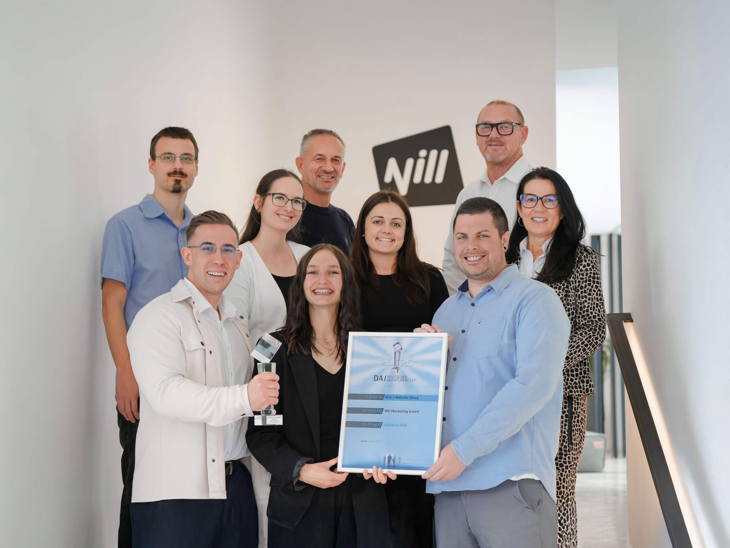 9 Personen lächeln mit Trophäe und Urkunde.