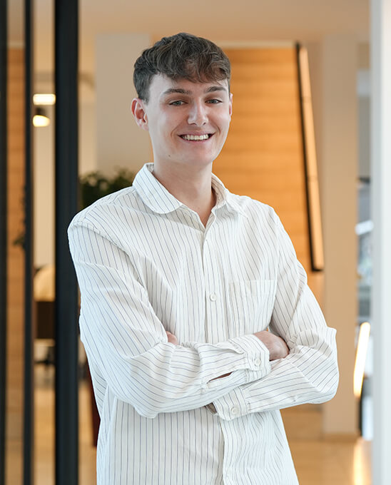 Junger Mann im gestreiften Hemd lächelt, Arme verschränkt.